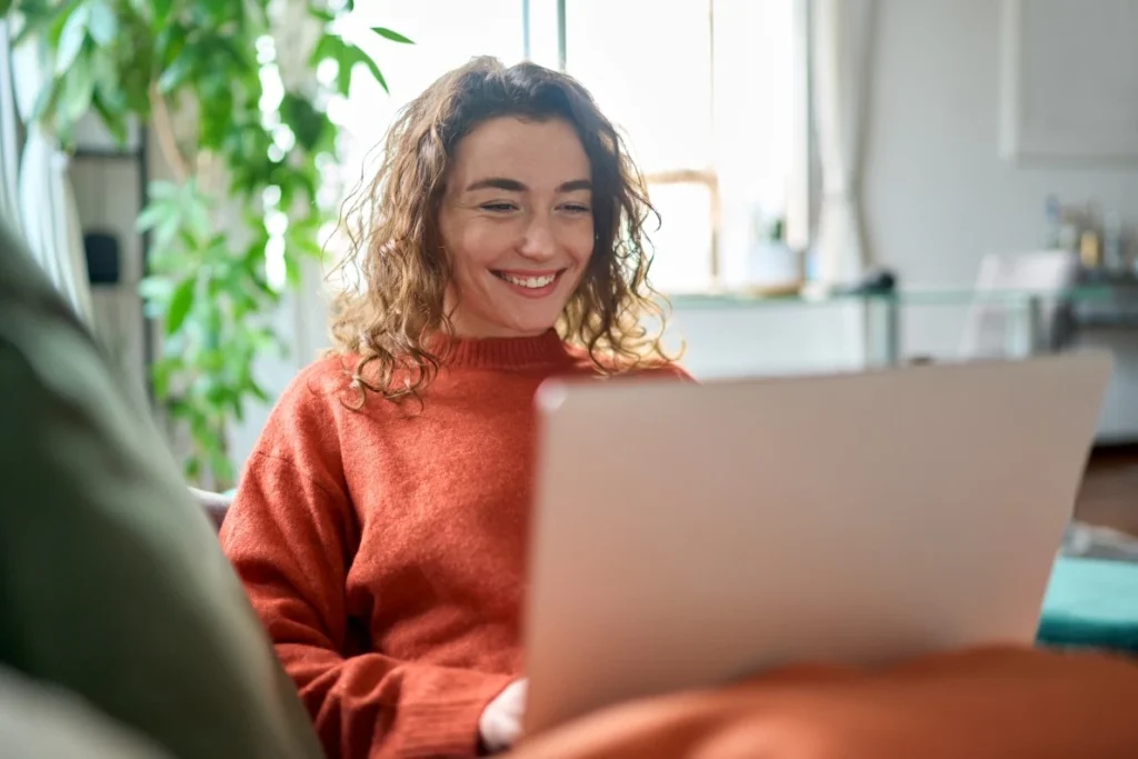 Happy woman sitting on couch using laptop to make an NDIS referral