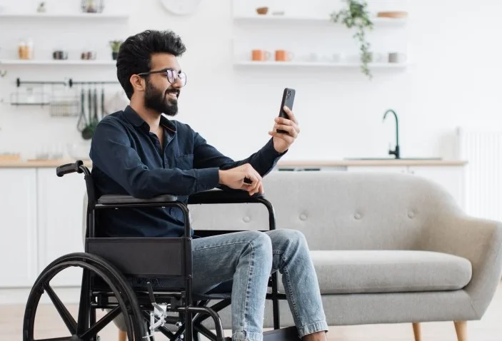 Disabled man in wheelchair sitting in living room looking at mobile phone
