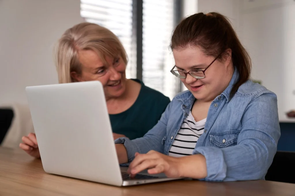 Plan Manager sitting with disabled woman with down syndrome looking at laptop together